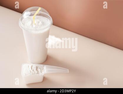 Molkenproteincocktail in einer Einweg-Tasse und Schaufel von Kollagen-Pulver auf einem beigen Hintergrund. Kollagen Peptide trinken für Gelenke und Schönheit. Protein Shake in Take Away Tasse. Stockfoto