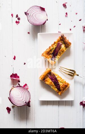 Gesalzener Kuchen mit Frühlingszwiebeln gestreift, mit Fontina, Eier, Sahne, und Würstchen, Violett stripses oben, rechteckigen Formen auf einem dunklen Hintergrund Stockfoto