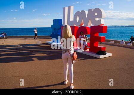 NICE, FRANCE-MAY,29,2019: Tourist poses for a photo near the I love Nice Tourist sign Installation above Promenade des Anglais in City of Nice Stockfoto