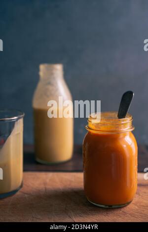 Pumkpin und Tomatensuppe auf einem Glasgefäß auf einem Holzschneider über einem rostigen Hintergrund, mit einer Kartoffelsuppenflasche im Hintergrund, Stockfoto