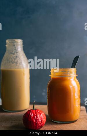 Pumkpin und Tomatensuppe auf einem Glasgefäß auf einem Holzschneider über einem rostigen Hintergrund, mit einer Kartoffelsuppenflasche im Hintergrund, Stockfoto