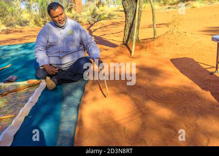 Kings Creek Station, Northern Territory, Australien - 21. Aug 2019: aborigine Guide man schafft Formen mit rotem Sand auf dem Boden in Aborigine-Kunst Stockfoto