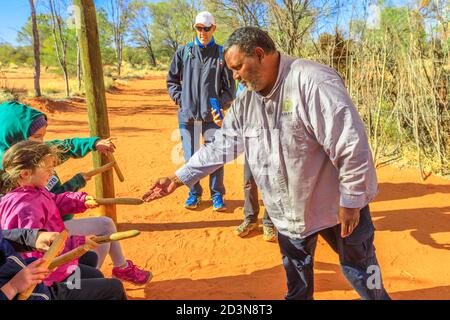 Kings Creek Station, Australien - 21. Aug 2019: aborigines Australischer Mann zeigt ein hölzernes Schlagzeuginstrument, das von Luritja und Pertame Leuten benutzt wird Stockfoto