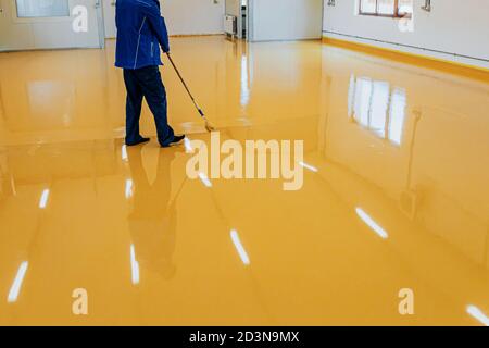 Arbeiter, Beschichtungsboden mit selbstnivellierenden Epoxidharz in der Industriewerkstatt. Stockfoto