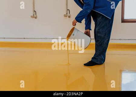 Arbeiter, Beschichtungsboden mit selbstnivellierenden Epoxidharz in der Industriewerkstatt. Stockfoto