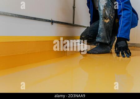 Arbeiter, Beschichtungsboden mit selbstnivellierenden Epoxidharz in der Industriewerkstatt. Stockfoto