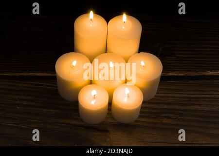 Gruppe von sieben brennenden Kerzen mit schwarzem Hintergrund. Konzept von Trost, Spiritualität, Mystik, Religion, Erinnerung an die Toten. Tag der Toten. Stockfoto