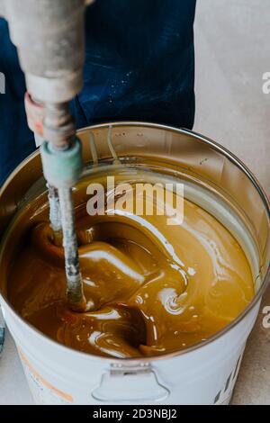 Arbeiter mischen gelbe Epoxidharz mit dem Mischer in einem Zinn-Eimer Stockfoto
