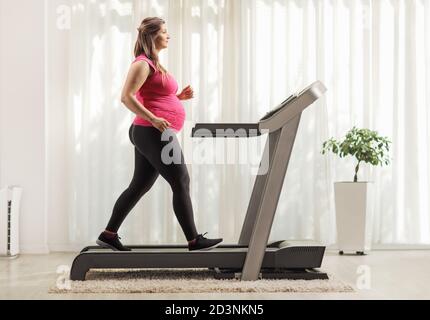 In voller Länge Profilaufnahme einer schwangeren Frau beim Training auf Ein Laufband zu Hause Stockfoto