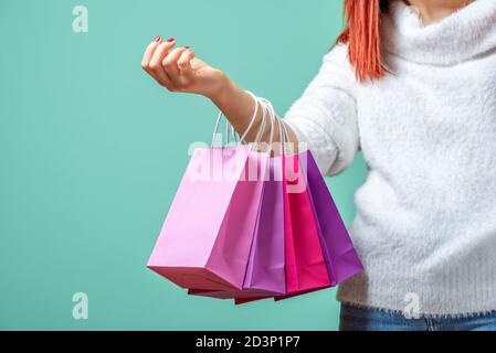 Junge rothaarige Frau, die farbige Einkaufstaschen an einem Arm hält. Eine Frau in einem weißen Pullover mit rosa und lila Papiertüten gekleidet. Stockfoto
