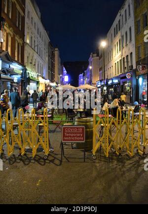 Menschenmenge in der Nacht auf der Old Compton Street mit Covid-19 Verkehrsbeschild, Soho, London 2020. Teile von Soho wurden für den Verkehr gesperrt, um vorübergehende Sitzgelegenheiten im Freien für Bars und Restaurants zu ermöglichen, um die soziale Distanzierung während der Pandemie zu erleichtern. Stockfoto