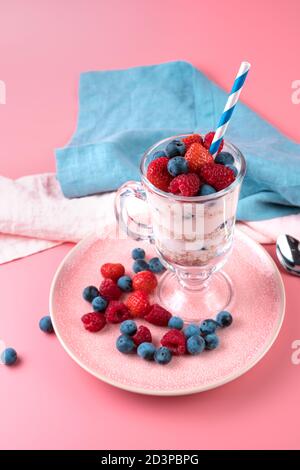 Creme mit Beeren und Müsli in einem transparenten Glas auf einem weichen rosa Hintergrund. Stockfoto