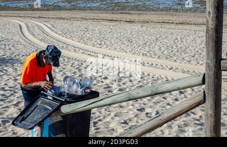 Verschwommener Vordergrund eines Müllwagenarbeiters beim Leeren des Mülls. Selektiver Fokus auf den Strand im Hintergrund. Stockfoto