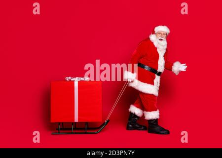 Oh nein, du hast mich gefunden. Foto-Porträt von stauned beeindruckt stilvollen weihnachtsmann mit weißem Bart ziehen große eingewickelte Geschenkbox auf Schlitten isoliert auf Stockfoto