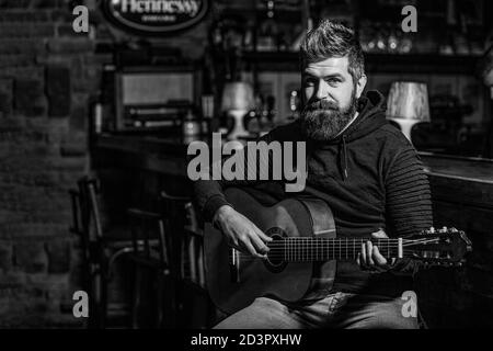 Spielen Sie die Gitarre. Bart Hipster Mann sitzt in einem Pub. Musikkonzept. Bärtiger Gitarrist spielt. Schwarz und Weiß Stockfoto