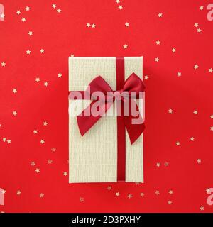 Geschenk in einer Schachtel mit Schleife auf rotem Hintergrund mit Konfetti. Draufsicht, flach liegend. Stockfoto