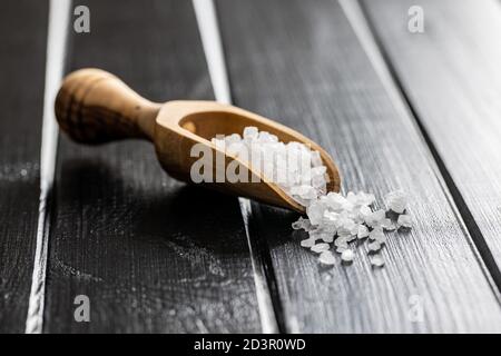 Weißes grobes Salz in Holzlöffel auf schwarzem Tisch. Stockfoto