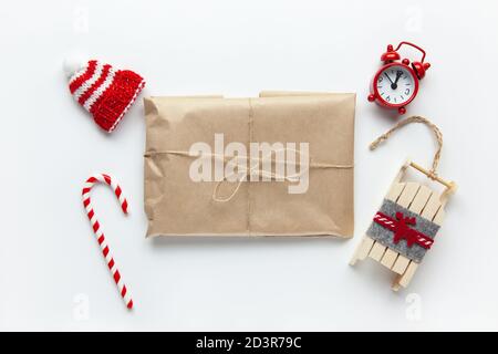 Weihnachten Geschenk verpackt in braun Handwerk Papier, mit der geissel gebunden, mit Zuckerrohr Süßigkeiten, kleine analoge Uhr, Schlitten, Hut auf weißem Hintergrund. Minimalistischer Stil. Top Stockfoto