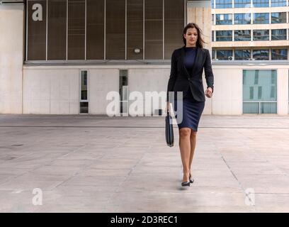 Schöne Geschäftsfrau verlassen Büro mit zu Fuß selbstbewusst in elegant gekleidet Anzug und Aktentasche Stockfoto