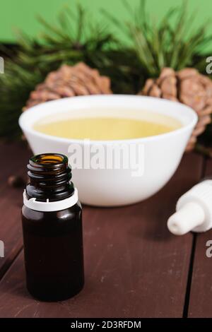 Zedernöl in einer Glasflasche und Zedernkegel mit Nüssen auf einem alten Holztisch. Stockfoto