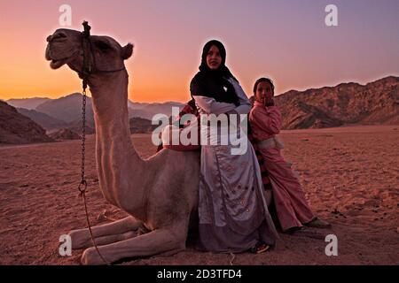 Eine Frau mit einem jungen Mädchen, das auf einem ruhenden Kamel lehnt. Im Hintergrund der Berg Sinai Stockfoto