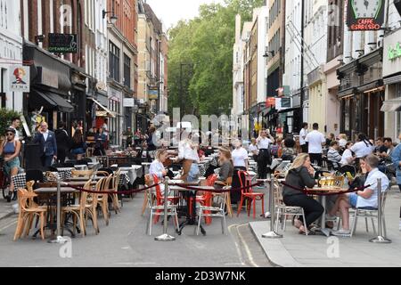 Menschenmenge in Bars und Restaurants in der Frith Street, Soho, London 2020. Teile von Soho wurden für den Verkehr gesperrt, um vorübergehende Sitzgelegenheiten auf der Straße und Tischservice im Freien zu ermöglichen, um die soziale Distanzierung während der Pandemie zu erleichtern. Stockfoto