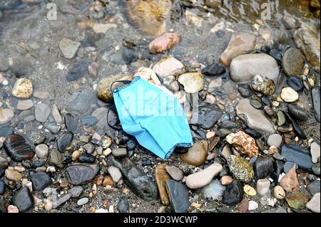 Eine blaue Gesichtsmaske aus Baumwolle wird auf dem abgelegt Strand, wenn es in einen Abfall hätte geworfen werden sollen Behälter Stockfoto