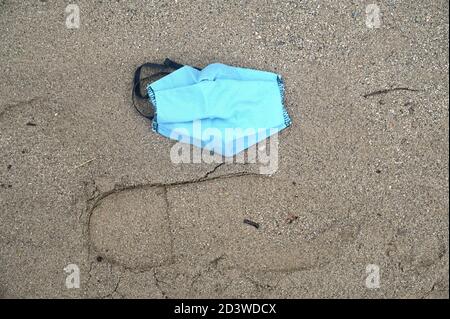 Eine blaue Gesichtsmaske aus Baumwolle wird auf dem abgelegt Strand, wenn es in einen Abfall hätte geworfen werden sollen Behälter Stockfoto