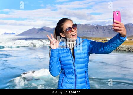 Island Tourist nimmt Selfie-Foto mit Smartphone auf Reise auf Island durch Jokulsarlon Gletscherlagune / Gletschersee auf Island. Fröhliches Touristenmädchen Stockfoto