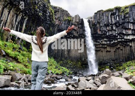 Island. Frau genießt majestätischen Svartifoss Wasserfall. Frau besucht berühmte Touristenattraktion von Island. Spektakuläres Naturdenkmal auf Stockfoto