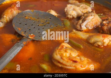 Detail eines Moments während der ersten Schritte des Kochens Eine Paella, in der Sie die Stücke von sehen können Fleisch und eine Schaufel, die hilft, die Zutaten zu bewegen Stockfoto
