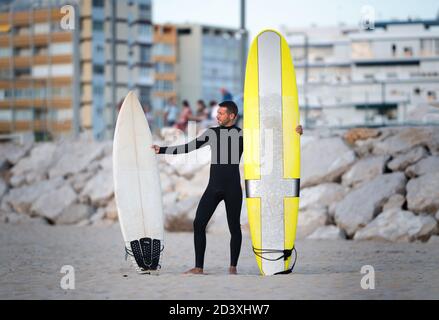 Portrait von Surfer in schwarz zipless Surfen Wetsuit versucht zu Wähle Longboard oder Shortboard Stockfoto