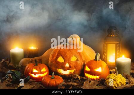 Jack o Laternen auf einem nebligen Hintergrund und mit trockenen Blättern, Kerzen und einigen anderen Kürbissen. Stockfoto