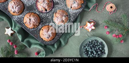 Heidelbeer-Muffins mit Zuckerguss in einem Backblech. Panoramabild von oben mit Weihnachtsdekor Stockfoto