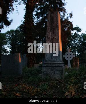 Ein alter Grabstein in einem alten Friedhof während des Sonnenuntergangs.die Sonnenstrahlen sind auf der Seite des Grabes. Stockfoto