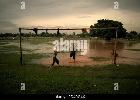 Kinder spielen Fußball auf einem teilweise überfluteten Feld, das sich zwischen zwei öffentlichen Friedhöfen in Pondok Kelapa, Jakarta, Indonesien, befindet. Stockfoto