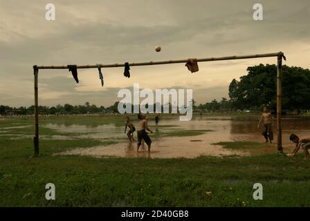 Kinder spielen Fußball auf einem teilweise überfluteten Feld, das sich zwischen zwei öffentlichen Friedhöfen in Pondok Kelapa, Jakarta, Indonesien, befindet. Stockfoto