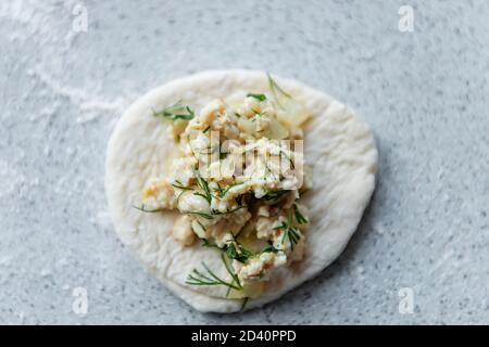 Eine der Stufen der Herstellung von Fleischknödel - auf Der Tisch auf einem Stück Teig ist ein Fleisch Füllung mit Grün neben einem Mehlhügel Stockfoto