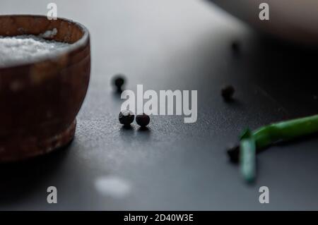 Kochen Gewürze - Meersalz in einem Holzbehälter schwarzer Erbsenpfeffer auf dem Tisch. Selektiver Fokus auf Vorder- und Rückseite Stockfoto