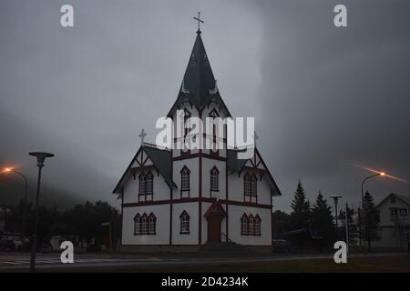 Húsavíkurkirkja, Husavik Holzkirche an einem nebligen Abend in Skjalfandi Bay, Nordost Island. Straßenlaternen leuchten bei gruseligen Wetter orange. Stockfoto