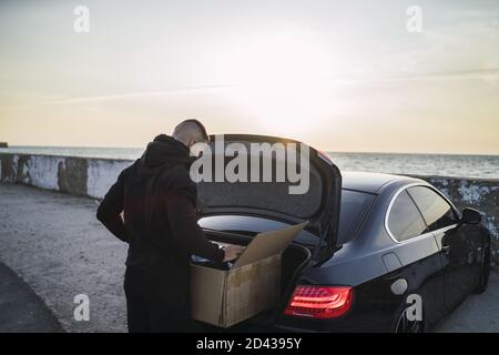 Junger Europäer, der ein Paket aus einem Kofferraum nimmt Stockfoto