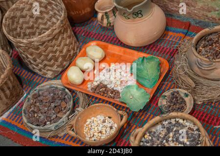 Farbenfroher Teppich mit orangefarbenem Teller, Tontöpfe, Stroh, Behälter mit verschiedenen Getreidearten und traditionellem Essen, Korbkorb, Nahaufnahme Stockfoto