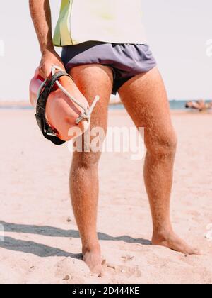 Vertikale Aufnahme von haarigen Beinen eines Rettungsschwimmer hält ein Orange Rettungsschlauch beim Stehen am Strand Stockfoto