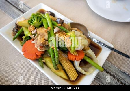Gebratenes gemischtes Gemüse in einem wunderschön dekorierten weißen Teller, Essen auf einem Holztisch, von oben betrachtet. Stockfoto