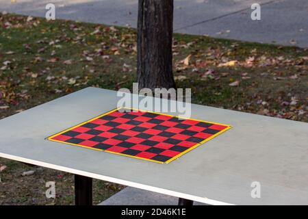 Schachbrett Spiel Hintergrund auf einem Metall Picknick-Tisch in einem Öffentlicher Park mit verstreuten Blättern auf dem nahe gelegenen Gras Stockfoto