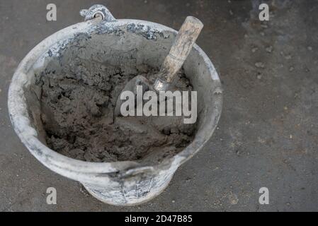 Die Putzkelle mischte den Zement im Eimer auf dem Zement Boden auf der Baustelle Stockfoto