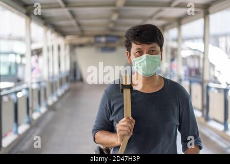Asian Mann tragen chirurgische Gesichtsmaske zum Schutz Coronavirus, covid19, Tragen einer Umhängetasche zu Fuß auf dem Skywalk nach der Fahrt mit dem Skytrain in Bangkok Stockfoto