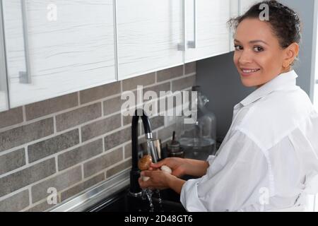 Die junge Köchin wäscht Pilze unter dem Wasserhahn und schaut uns an. Stockfoto