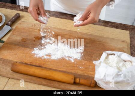 Nahaufnahme der Hände des Küchenchefs, der Mehl auf das Holzbrett streut. Stockfoto