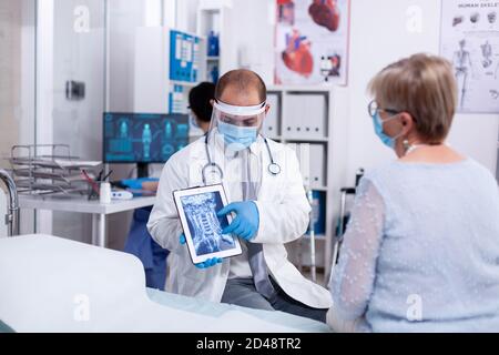 Arzt im Krankenhauszimmer erklärt Röntgen auf Tablette für ältere Frau während der Konsultation im Klinikraum. Medizinische Untersuchung auf Infektionen, Krankheit und Diagnose. Stockfoto